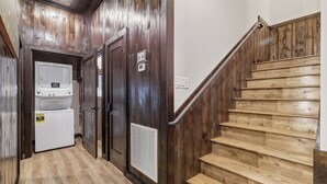 Eine Holztreppe führt zu einer Zwischenebene mit einem Waschraum, der zwei Trockner und eine Lüftungsanlage beinhaltet.