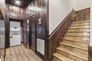 A wooden staircase leading to a landing with a laundry room featuring two dryers and a vent. - New Host Special • Indoor Pool • Glow Court • Golf Sim • Rooftop Hot Tub • Sauna (Pigeon Forge)