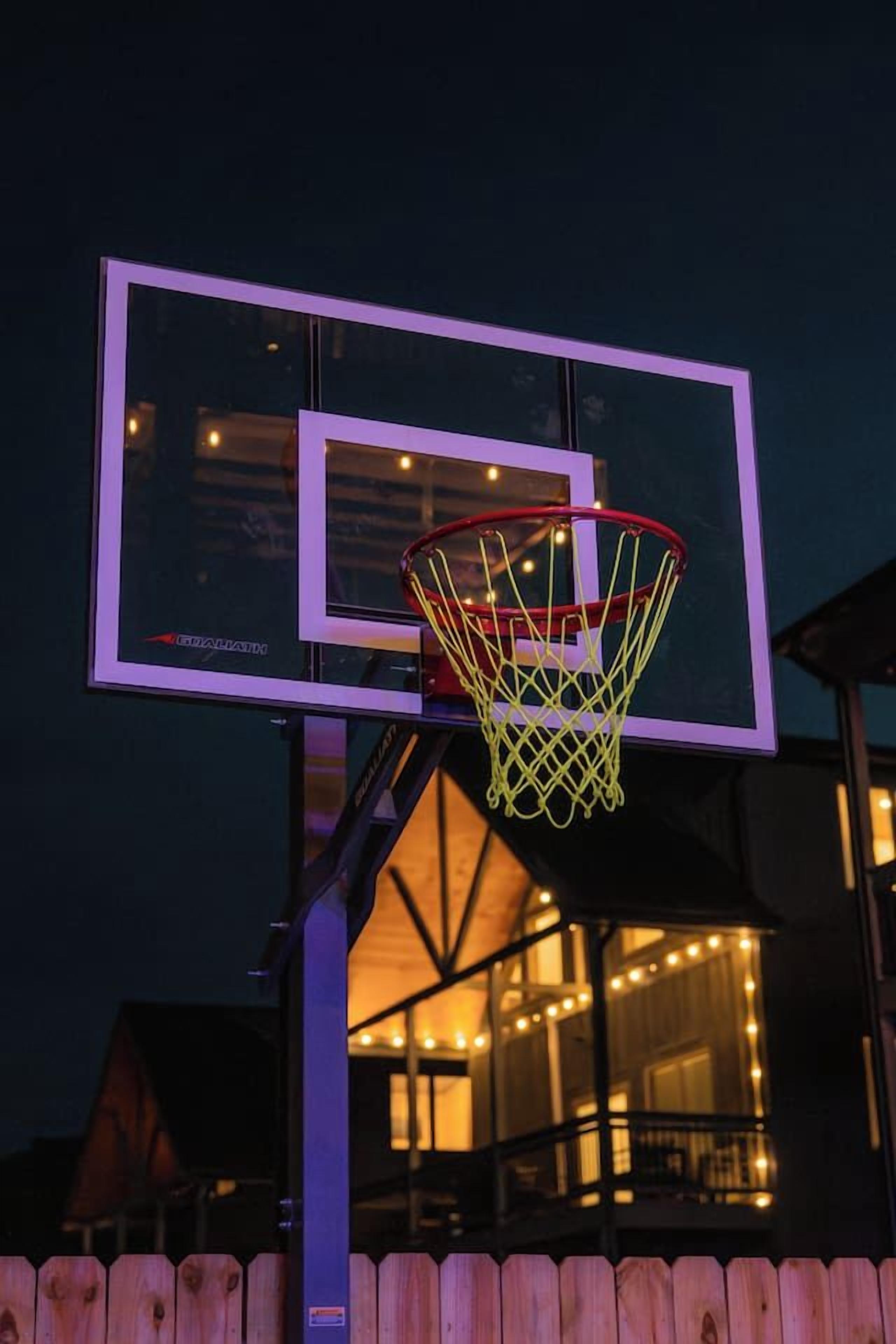 A basketball hoop with a net, mounted on a metal pole, with a wooden fence in the foreground.