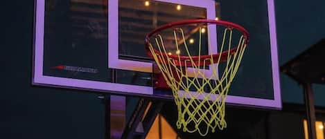 A basketball hoop with a net, mounted on a metal pole, with a wooden fence in the foreground.