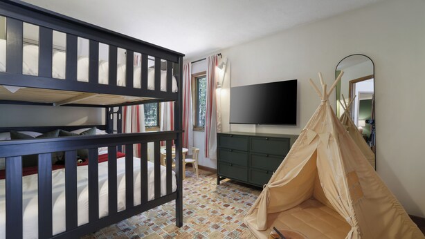Une chambre avec un lit superposé, une commode, un téléviseur et une tente indienne.