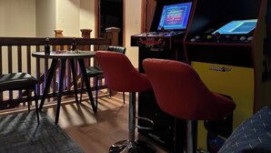 Une pièce avec des bornes d’arcade, une table avec des chaises et un banc en bois.