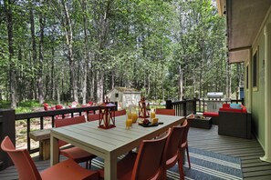 Terraza al aire libre con mesa lista para comer, rodeada de sillas rojas, con vistas a un área boscosa.