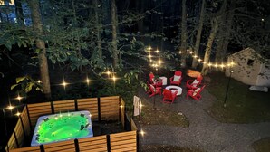 Un bain à remous entouré de bancs en bois et de chaises rouges, installé dans un jardin illuminé de guirlandes lumineuses.