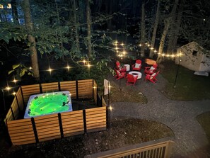 Ein Whirlpool, umgeben von hölzernen Bänken und roten Stühlen, inmitten eines Gartens mit Lichterketten.