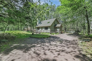 Eine Hütte mit Veranda, umgeben von Bäumen, und einer Schotterauffahrt, die zum Eingang führt.