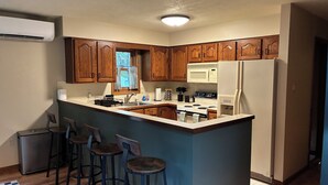 A kitchen with wooden cabinets, a central island with stools, a refrigerator, and a microwave.