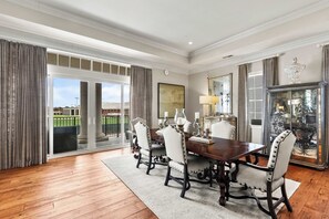 Een eetkamer met een grote tafel, stoelen en een uitzicht door glazen deuren op een balkon.