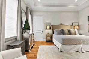Un dormitorio con cama, mesitas de noche, cómoda, espejo y ventana con cortinas.