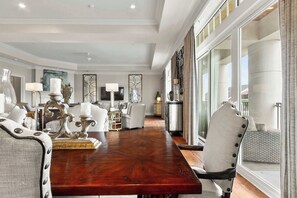 Une salle à manger spacieuse, avec une longue table en bois, des chaises rembourrées et une vue dégagée grâce à de grandes portes vitrées.