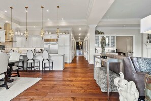 Una cocina amplia con armarios blancos, un comedor con mesa y sillas, y una sala de estar con sofá y objetos decorativos.