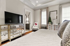 Ein Schlafzimmer mit einem großen Bett, einem Fernseher, einer Kommode und einem Sessel.