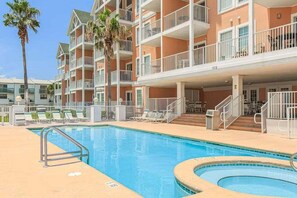 A hotel with a swimming pool, multiple balconies, and a palm tree. - Beachfront Gulf Shores condo with ocean view, pool, hot tub & balcony. (Gulf Shores)