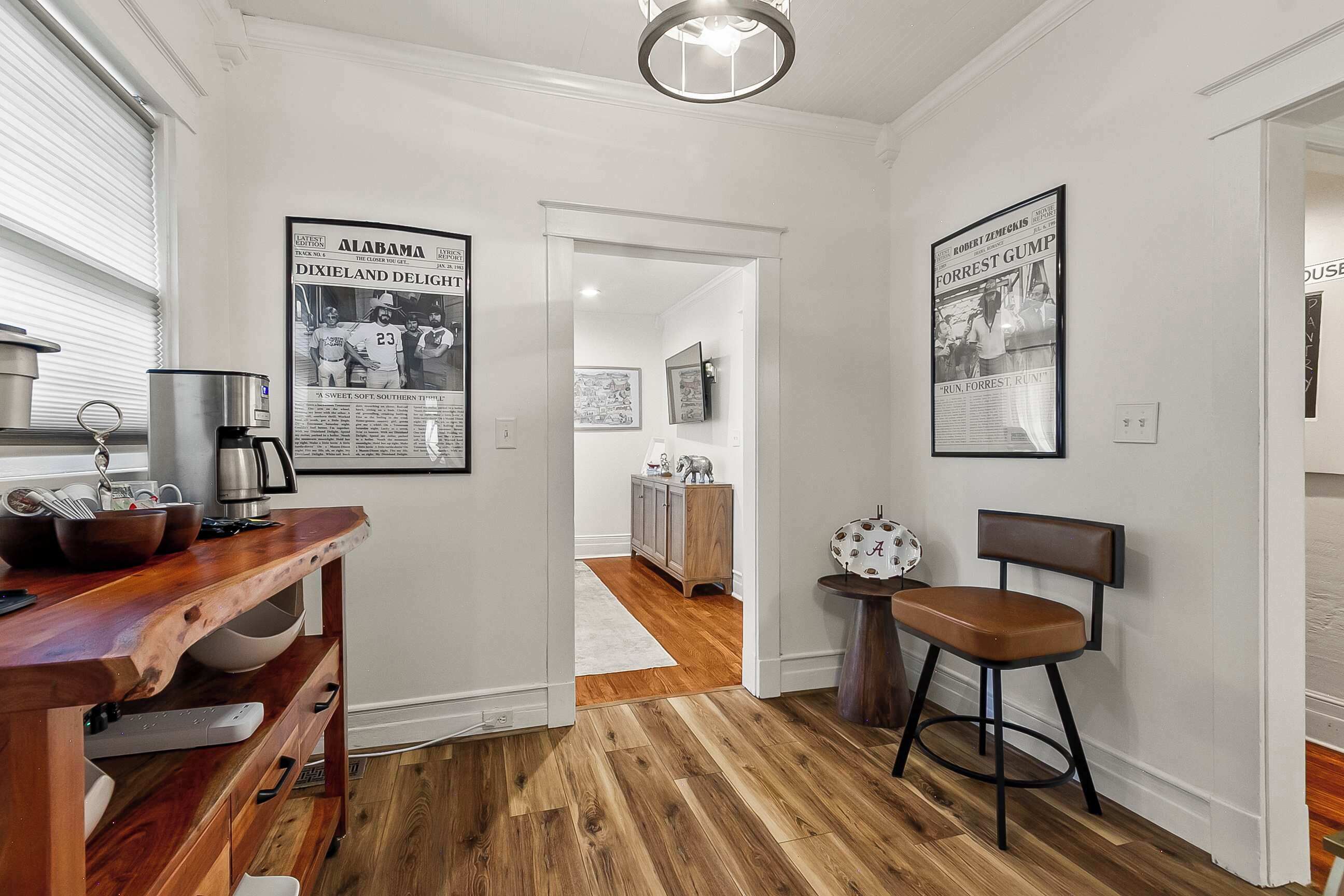 A hallway with wooden flooring, a dining area with a wooden table and chairs, and framed newspaper articles on the walls.