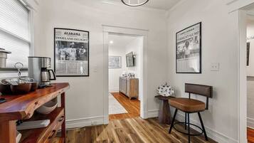 A hallway with wooden flooring, a dining area with a wooden table and chairs, and framed newspaper articles on the walls.