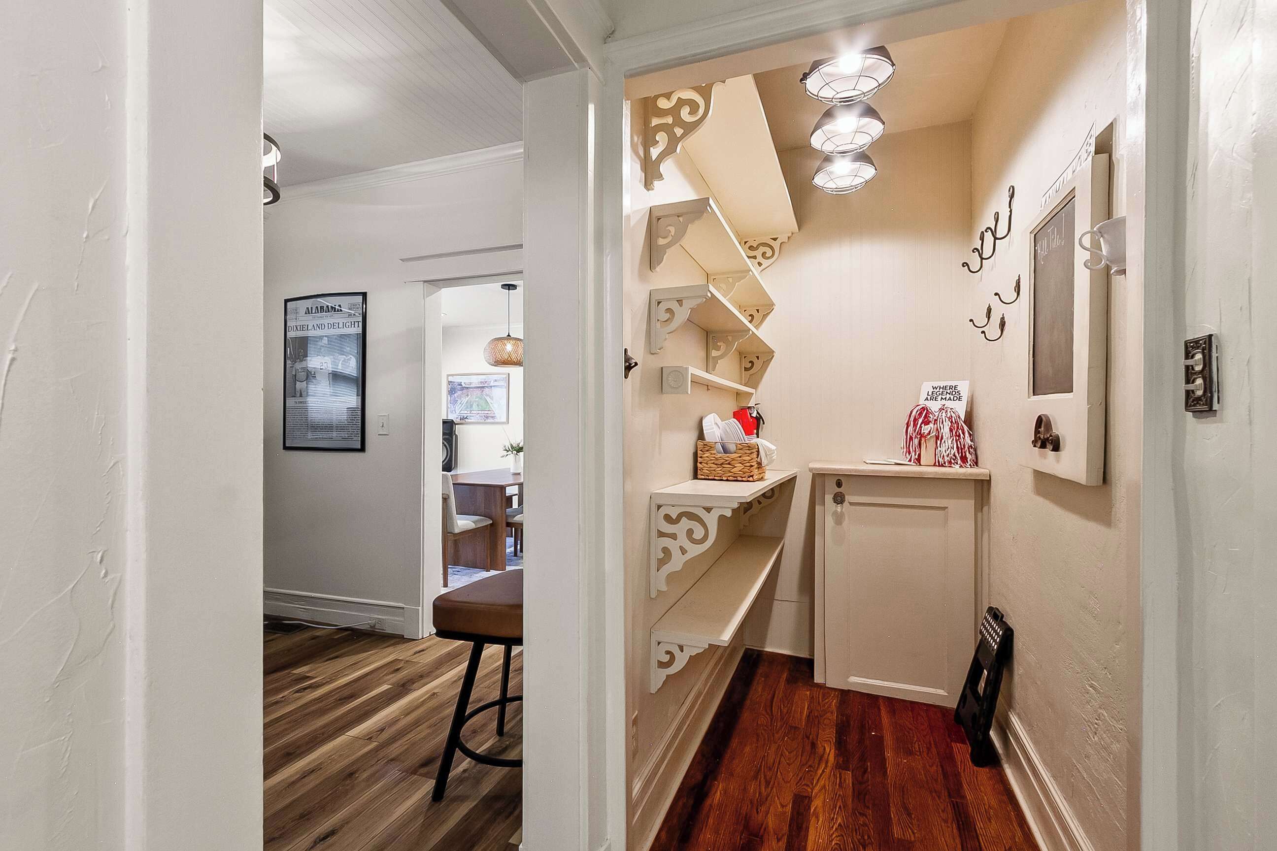 Un couloir doté d’un plancher en bois, d’une porte blanche et d’une petite armoire blanche avec des étagères décoratives.