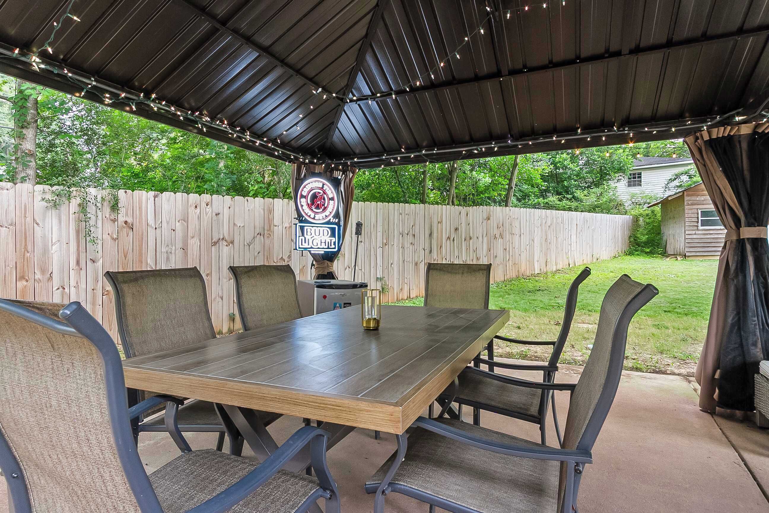 An outdoor patio with a covered table and chairs, a wooden fence, and a sign with a logo.