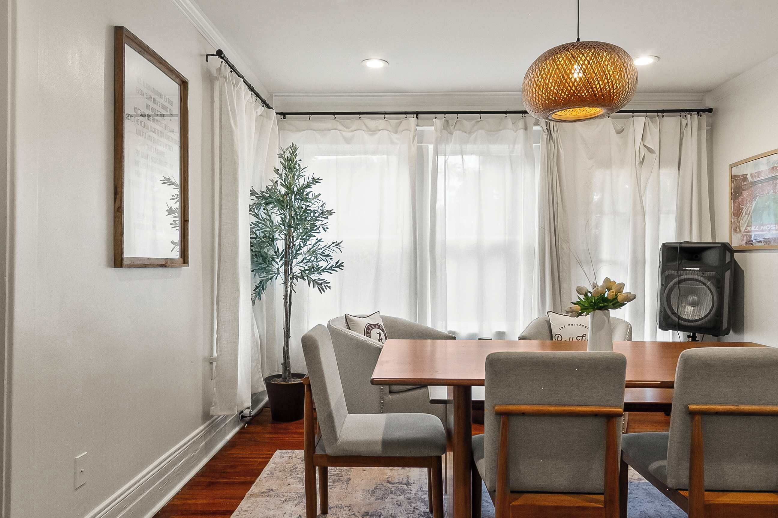 Un coin repas avec une table en bois, des chaises grises, une plante en pot et un haut-parleur.