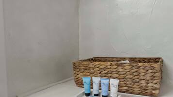 Un baño con un lavamanos blanco, un estante blanco y una cesta tejida con cuatro botellas de H2O.