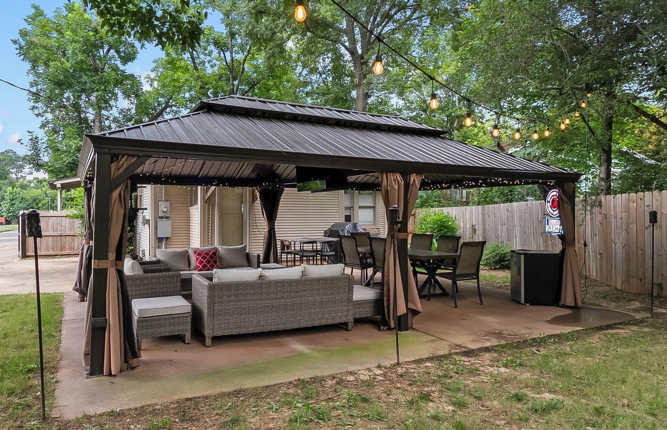 A covered outdoor seating area with a sofa and chairs, a grill, and a patio table.