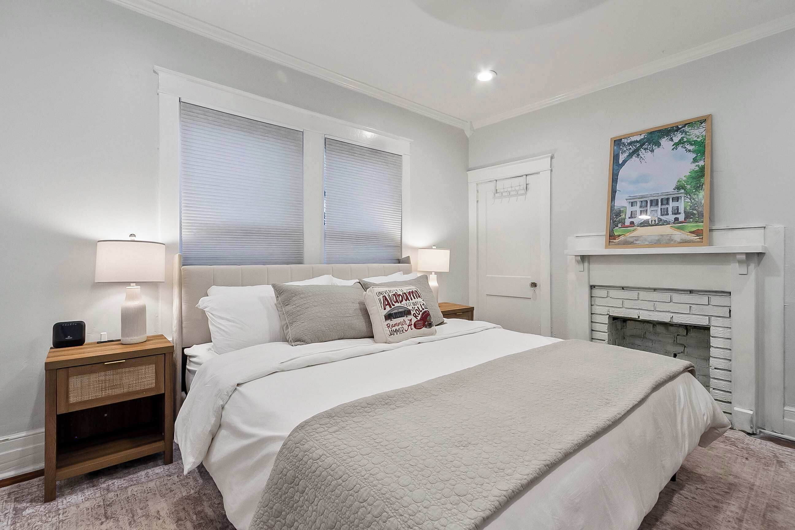 A bedroom with a bed, nightstands, a fireplace, and a painting on the wall.