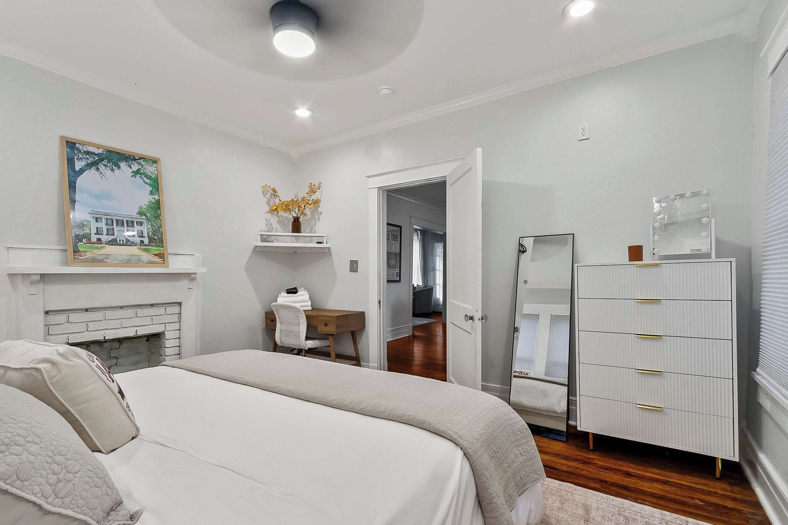 Une chambre à coucher comprenant un lit, une commode, un miroir, une cheminée et une porte donnant sur une autre pièce.