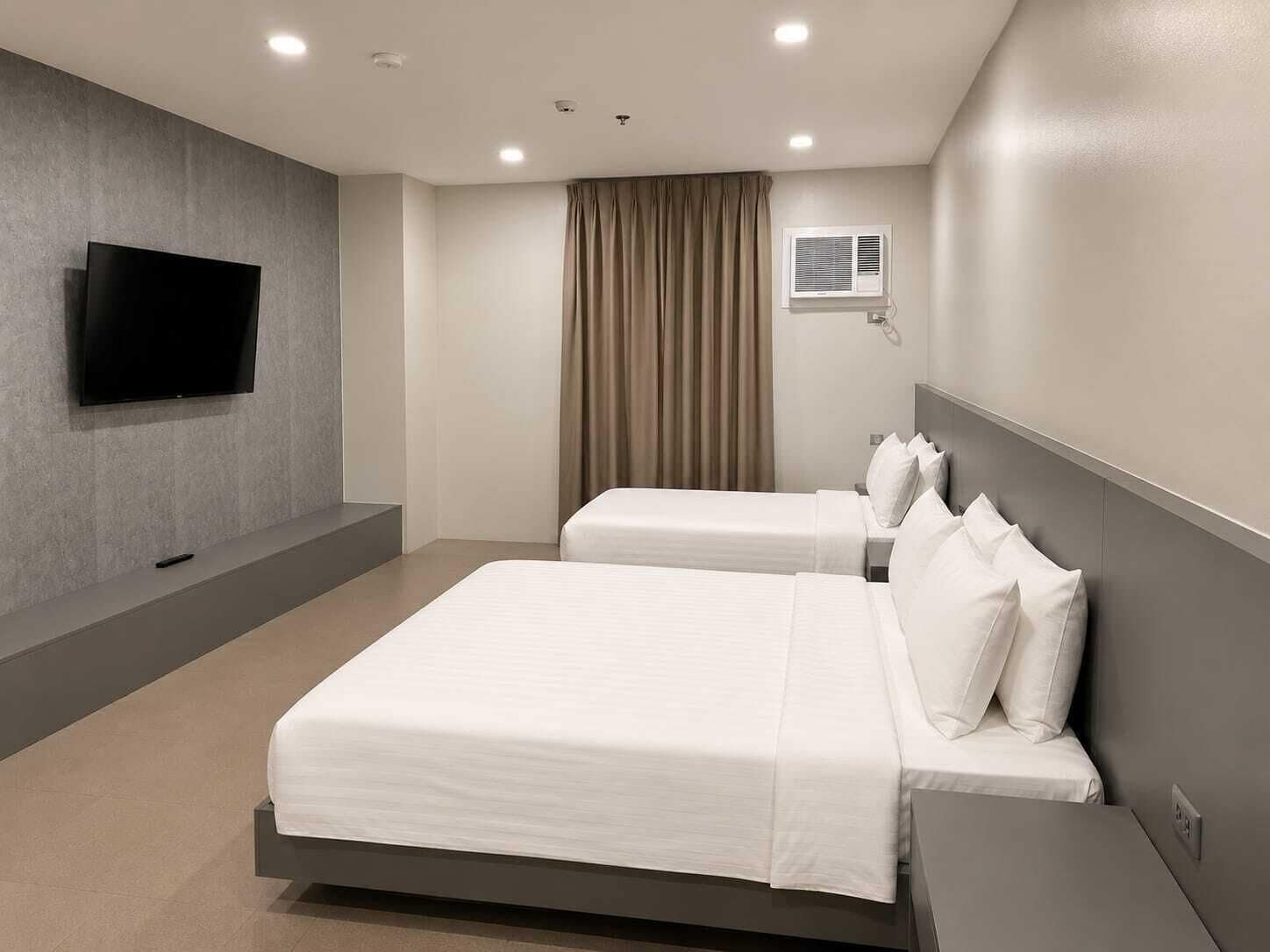 Une chambre d’hôtel avec deux lits, un téléviseur à écran plat fixé au mur, un appareil de climatisation et une fenêtre avec des rideaux.