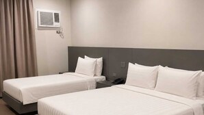 A hotel room with two beds, a bedside table with a phone, and a wall-mounted air conditioning unit.