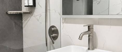 Une salle de bain moderne avec un lavabo blanc, une douchette à main et un miroir au-dessus du lavabo.