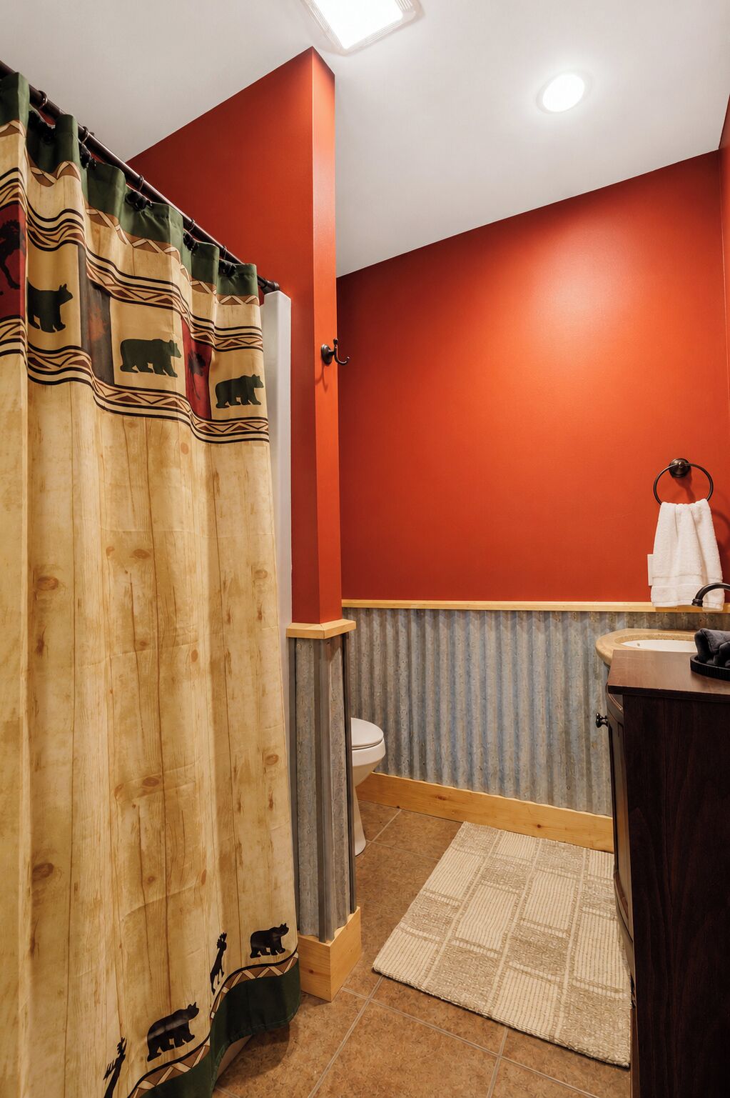 Ein Badezimmer mit Holzduschvorhang, Toilette, Waschbecken mit Handtuch und einem gemusterten Teppich.
