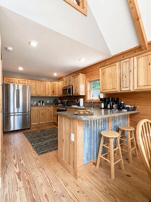 A modern kitchen with wooden cabinets, stainless steel appliances, and a central island with stools. - Long-Range Views on 3 Levels | Hot Tub + Fire Pit (Maggie Valley)