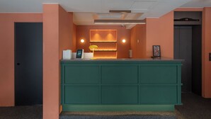 Un comptoir d’accueil avec un plan de travail vert, une horloge numérique et une étagère fixée au mur où sont exposés des objets en verre.