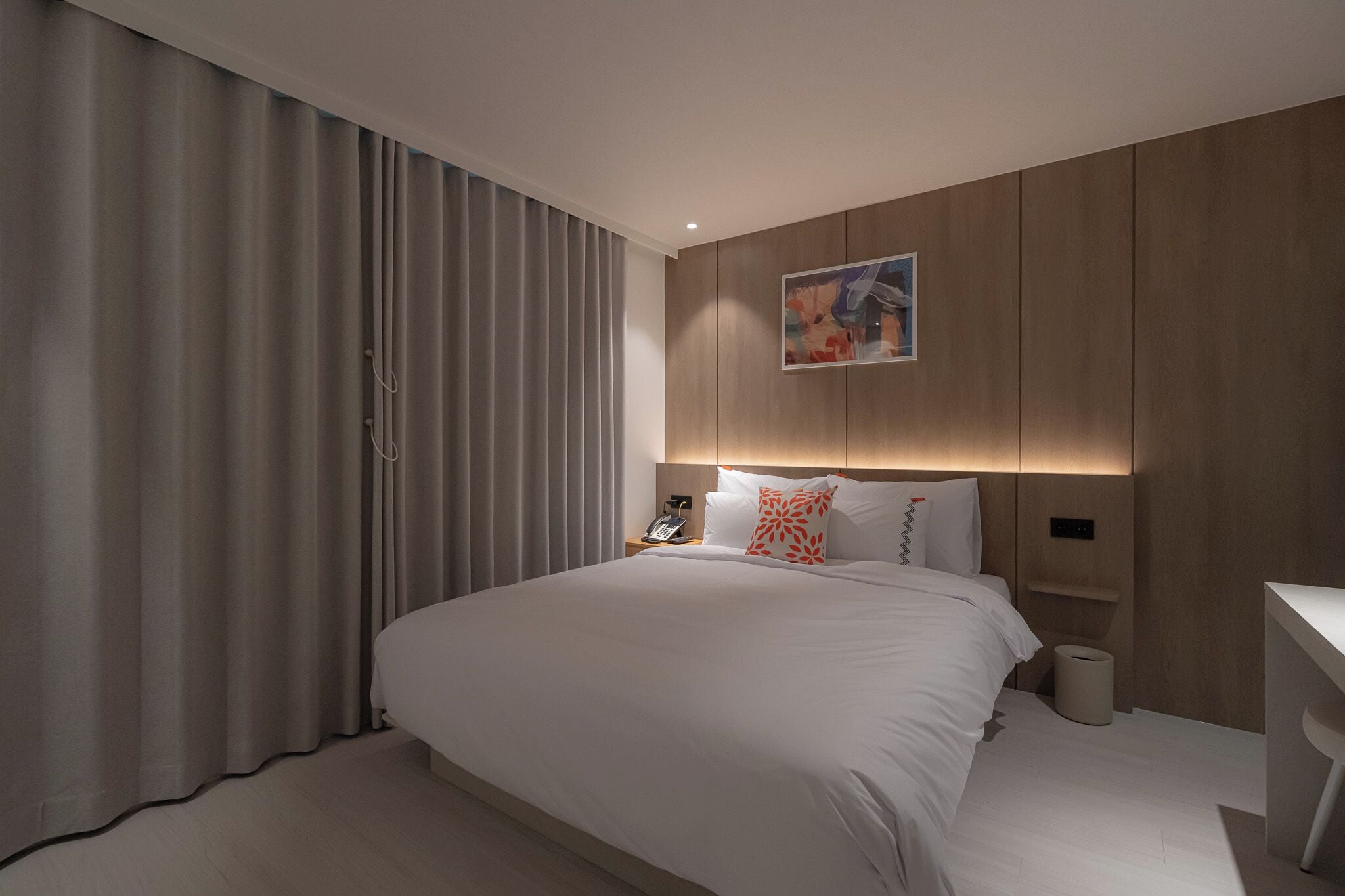 Et moderne hotelværelse med en stor seng, et sengebord, en telefon og en lampe monteret på væggen.