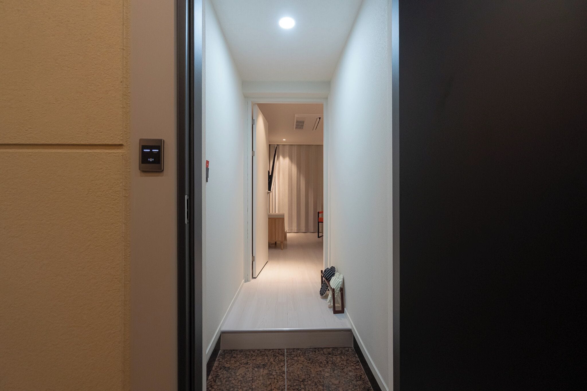 A hallway with a carpeted floor, a door on the left, and a light fixture on the ceiling.