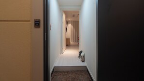 Un couloir doté d’un sol recouvert de moquette, une porte sur la gauche et un luminaire au plafond.