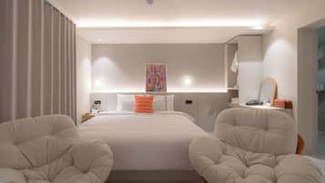 A modern hotel room with a large bed, two armchairs, a bedside table with a lamp, a painting on the wall, and a mirror above the table.