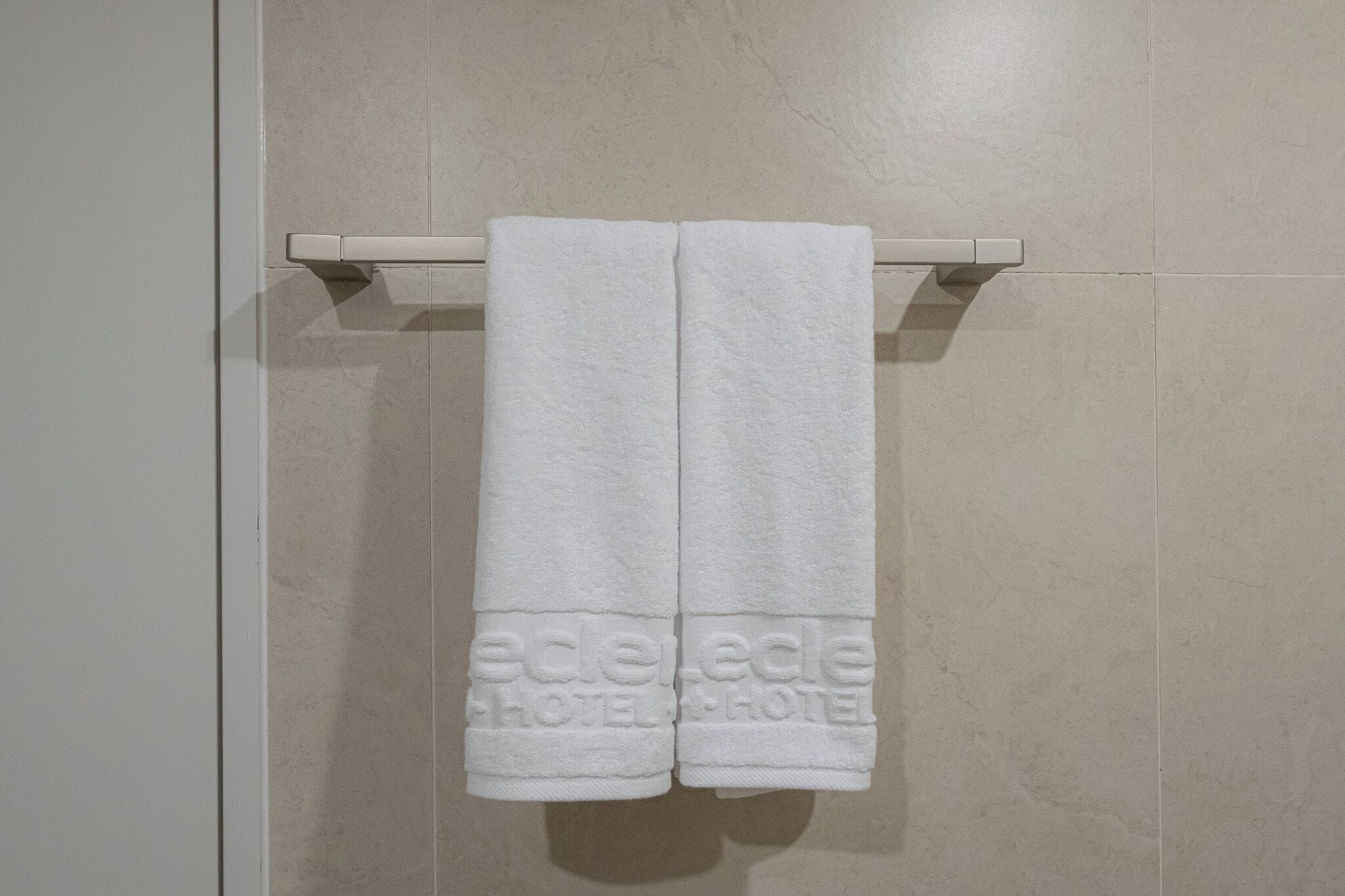 A pair of white towels hanging on a wall-mounted towel rack in a bathroom with a tiled floor.