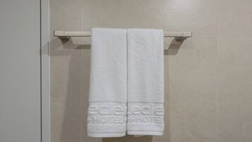 A pair of white towels hanging on a wall-mounted towel rack in a bathroom with a tiled floor.
