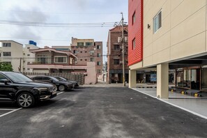 A parking lot with multiple cars, a building with a red facade, and other residential buildings in the background.