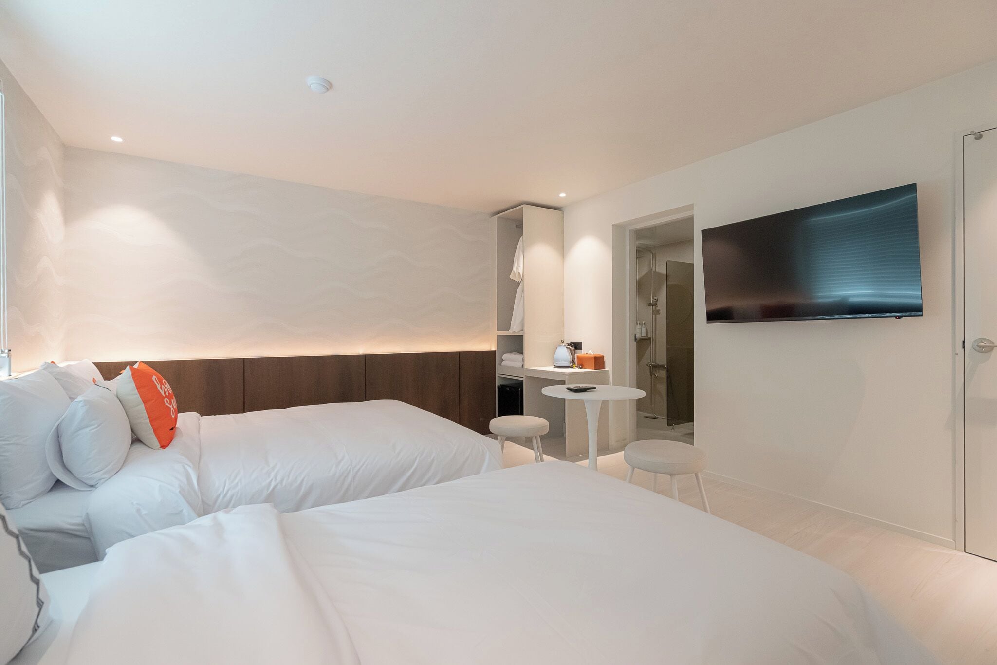 A modern hotel room with two beds, a small table, a TV, and a shower area.