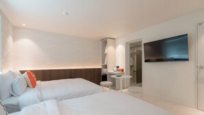 Une chambre d’hôtel moderne équipée de deux lits, d’une petite table, d’une télévision et d’un espace douche.