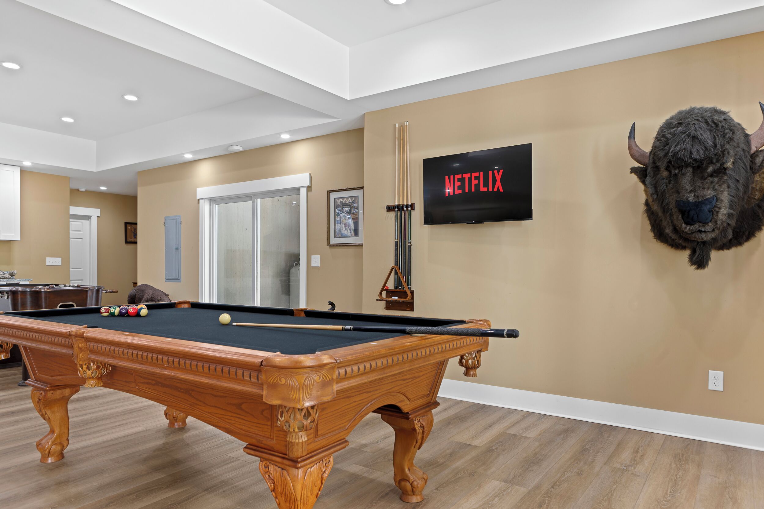 A pool table in a room with a mounted television displaying 'NETFLIX' and a mounted buffalo head decoration.