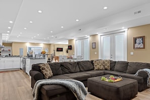 A modern living room with a sectional sofa, a coffee table with fruit, and a kitchen in the background.