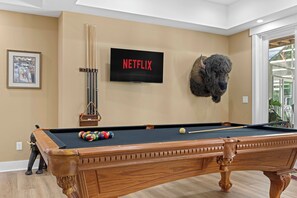 Una mesa de billar con un televisor montado que muestra el logotipo de Netflix, una cabeza de animal montada y un cuadro en la pared.