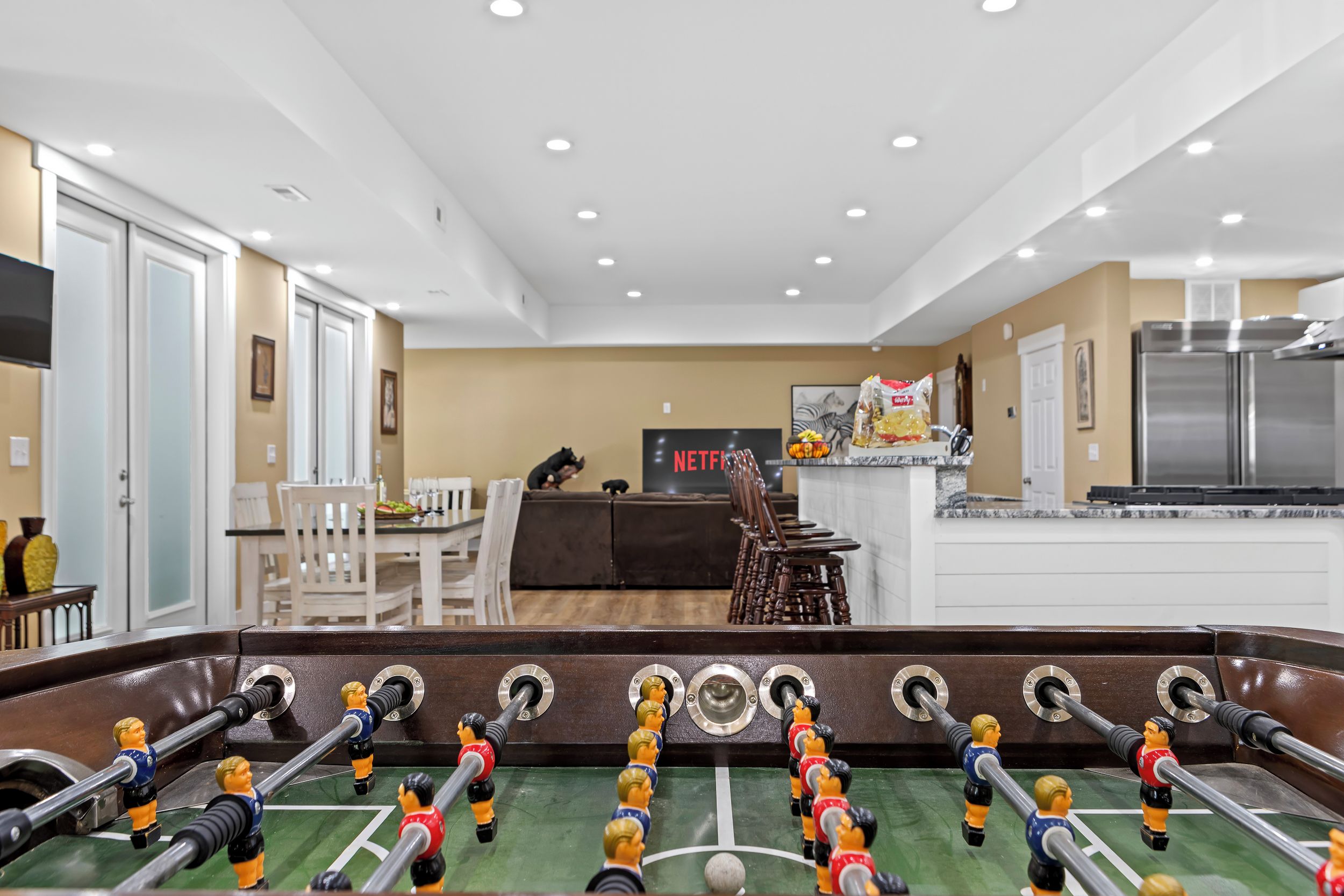 A modern living room with a foosball table, a dining area, and a kitchen with a refrigerator.