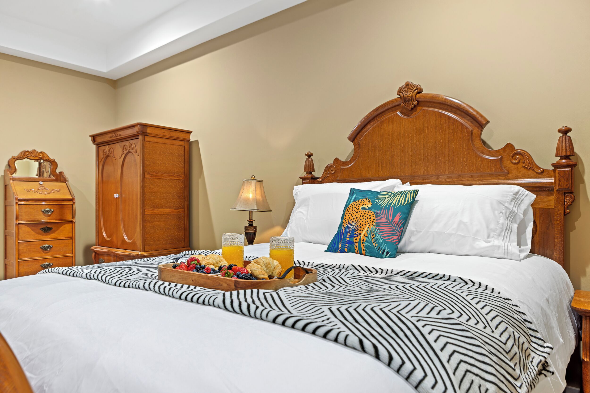 A hotel room with a large bed, a wooden nightstand, a dresser, and a lamp.