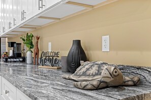 A kitchen with a marble countertop, a coffee machine, a vase, and a welcome sign.