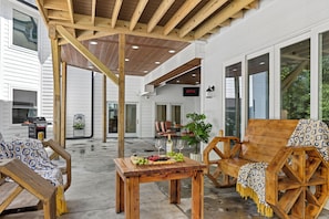 A covered outdoor seating area with wooden furniture and a table set for a meal.