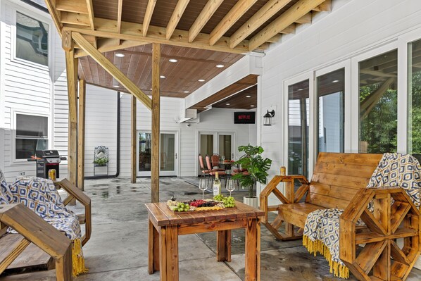 A covered outdoor seating area with wooden furniture and a table set for a meal.