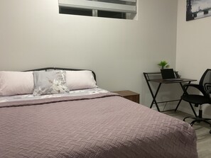A bedroom with a bed, a desk, a chair, and a window. - Comfortable modern basement suite (Winnipeg)